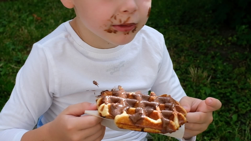 The child eating a Belgian waffle with a chocolate topping.top view. daily life dirty stain for wash and clean concept | Shutterstock HD Video #1076523524