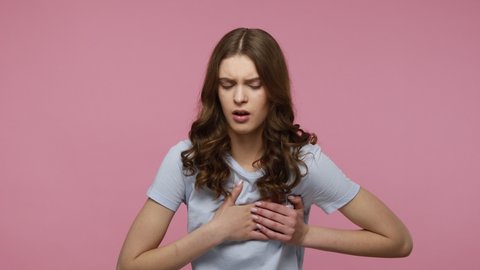 Infarction, cardiac problem. Adorable teenager girl grabbing chest and screaming from sudden sharp pain, heart attack, risk of breast cancer. Indoor studio shot isolated over pink background.