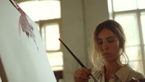 Beautiful woman artist creating abstract artwork at art workplace. Talented painter painting on canvas indoors. Focused female person working on picture at easel in art studio.