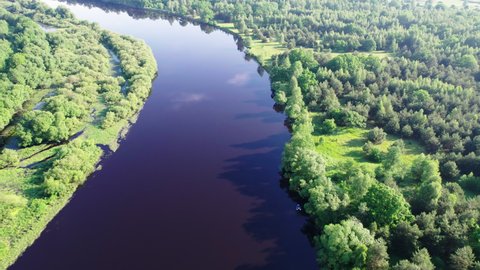 Flying over the bend of a dark-water river with tributaries in a wooded area. Aerial view