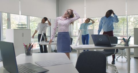 Cheerful diverse colleagues doing neck stretching exercise standing in office. Multiethnic young office employees do workout exercises during break at work