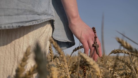 woman holding a christian cross walks in a wheat field 
