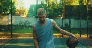 Male basketball player practicing ball handling skill, dribbling ball and throwing in camera on outdoor court in summer
