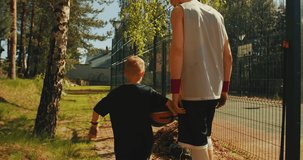 Basketball players male sportive guy and child boy going to workout together on basketball court outdoors in summertime