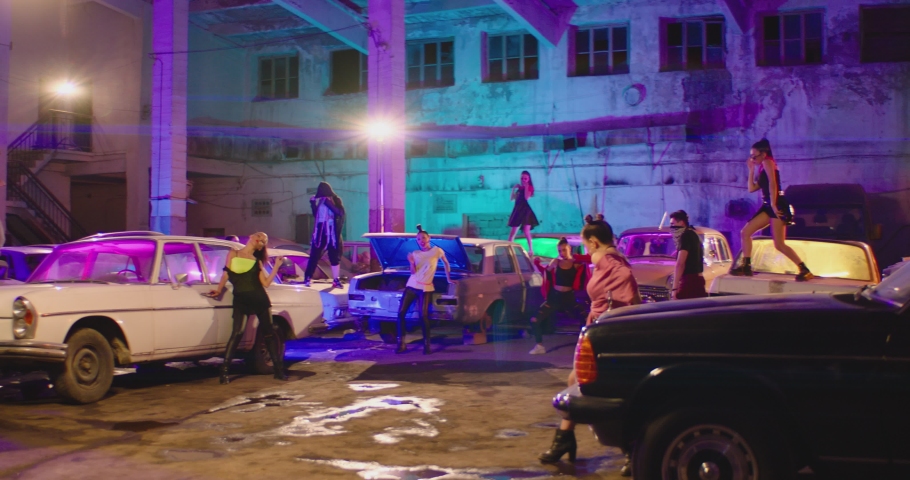 Group of stylish young people dancing , moving inside abandoned garage building . Old hippy style party . Colorful stylish clothes , african braids. Dancers on the car roofs , vintage broken old cars  | Shutterstock HD Video #1076543123
