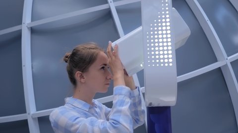 Observation, relax, sightseeing, astronomy, discover, education concept. Young woman in plaid shirt looking through white telescope, exploring exhibits at modern space exhibition, museum