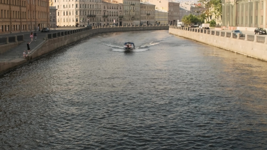 Ship floating by the steep bank, boat going away. water surface fluctuation. Small waves spreading out flowing water in the channel going through the city. the dark deep river. route ship with people.