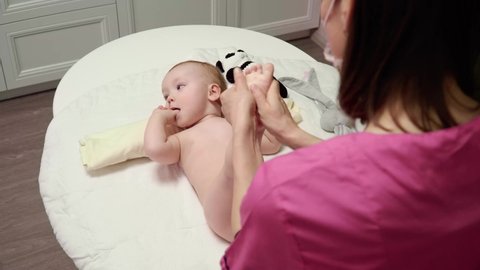 The masseuse gives a foot massage to a baby (boy). The baby lies on his back and sucks his thumb.
