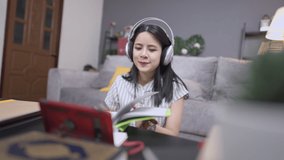 Young asian overjoyed woman excited about success, dancing while sitting learning at home on weekend, having an impressed time finish hard homework on time, using wireless headset and smartphone 