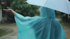 Asian woman wearing and spreading an umbrella a raincoat outdoors rainy day. Slow motion.
