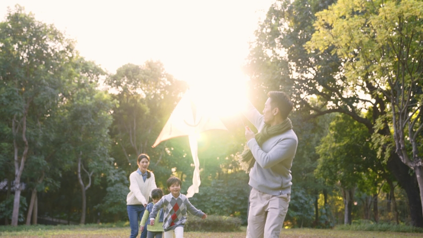 Happy asian family having fun flying a kite outdoors in park