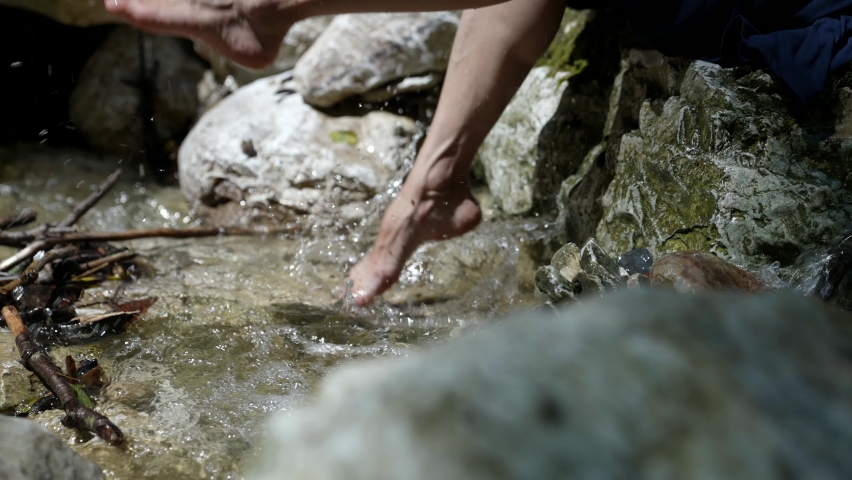 Close-up of female legs in slow motion playing with a stream of mountain clear water. Outdoor vacation in the open air. The concept of a healthy and happy lifestyle.