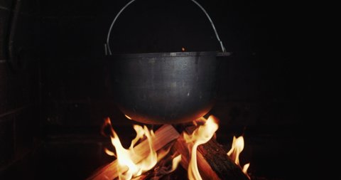 A cast-iron vat of boiling broth hangs in a wood-burning stove over an open fire. Slow motion video