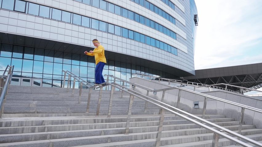 Parkour, young guy performs a backflip over obstacles in the city and doing a flip on training area near modern buildings, 4k slow motion.