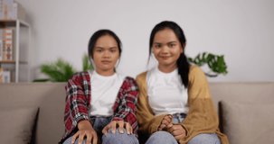 Portrait of Happy asian twin girls waving hand while sitting on couch at living room. Twin female smiling and looking at camera. Funny lady blogger waving hand. Lifestyle, online, video call concept.