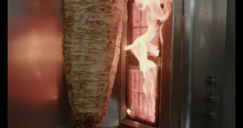 Cutting off roasting chicken meat shavings from vertical grill with sharp , long knife. Cooking Arabic Shawarma.