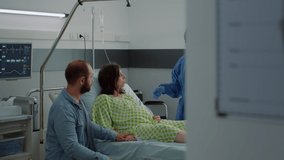 Caucasian couple expecting baby in maternity ward at hospital. Pregnant woman sitting in bed talking to african american nurse and young husband. Medical assistance for childbirth - Powered by Shutterstock - Get 15% off with code: PIKWIZARD15