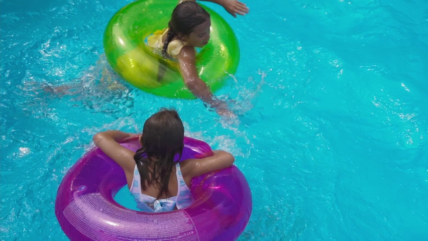 Funny two little girls sisters swim and Spinning into an inflatable circle. Children have fun and play, dives on the water pool in the summer on vacation, holidays, weekends with family | Shutterstock HD Video #1076575541