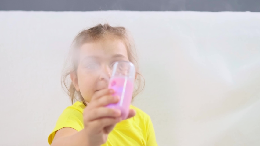 Little girl in yellow t-shirt sitting on the sofa holding in her hands humidifier and experiments with it right in front the video camera.