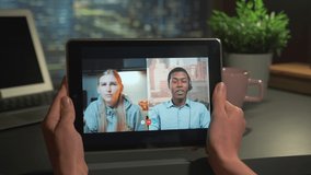 Online video meeting on tablet: mixed-race man and woman speaking about something. Female hands holding tablet.