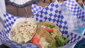 This panning video shows dishes filled with fish tacos and coleslaw at an outdoor restaurant with paper blowing in the wind.