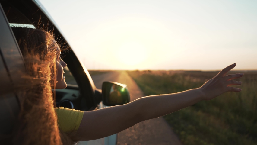Child in car window. Family car trip. Child hair in wind. Girl looks out of car window. Happy child travel with his family. Girl stretches out his hand to wind. Happy family travel concept by car | Shutterstock HD Video #1076589506