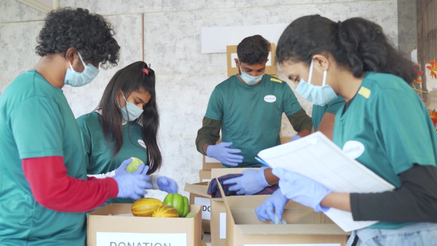 Group of volunteers working together by arranging cloths and vegetables with medical face mask during coronavirus or covid-19 pandemic. Royalty-Free Stock Footage #1076590709