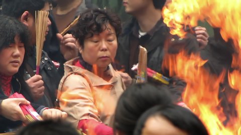 HANGZHOU, CHINA, CIRCA APRIL 2009, Lingyin Temple, Women and man lighting joss sticks seen through flames, smoke and heat shimmer 