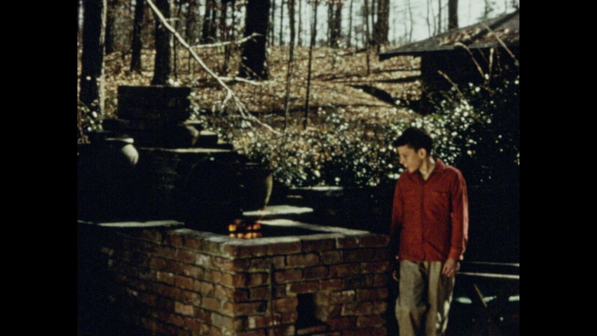 1950s: Boy standing by fire pit. Boy watching fire. Close up of boy, fire truck pulls up to building, firefighters set up equipment. Hand turns on stove.