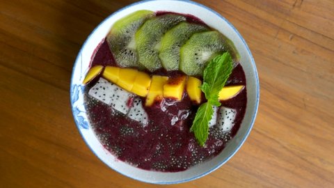 Woman Hand Eating Vegan Smoothie Bowl by Spoon with Fresh Fruits and Chia Seeds. Healthy Breakfast in Cafe. Vegetarian Meal with Tropical Fruits - Mango, Kiwi and Dragon Fruit. Acai Bowl. 4k