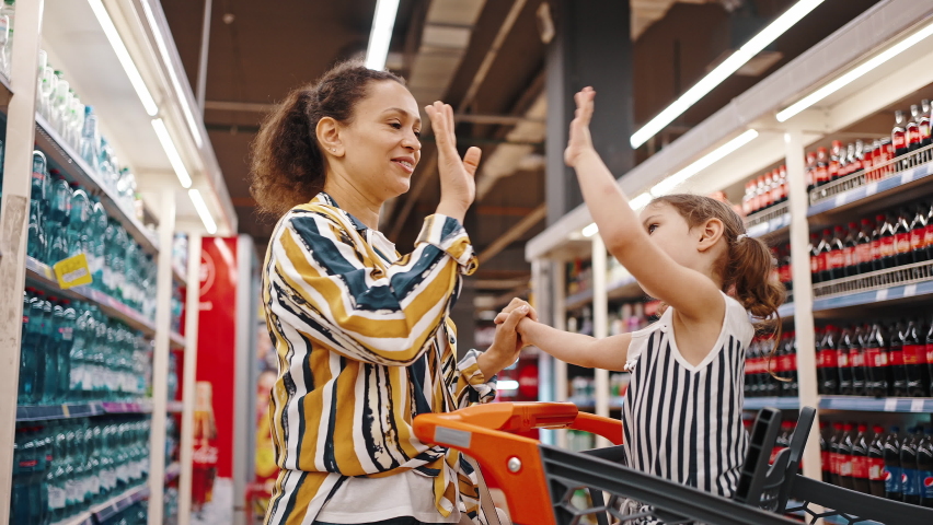 Well done, success concept. Girl sits in a supermarket trolley and claps her hands on her mother's hands. Family shopping, happy family. Royalty-Free Stock Footage #1076598716