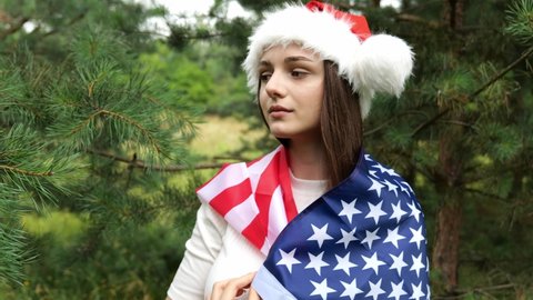 Young cute brunette girl in a New Year's cap with the flag of the usa on a green pine background. Forest, new year, holiday