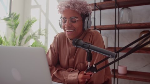 Attractive Young African American Woman Talking Into Microphone While Recording Radio Show Wearing headphones. Beautiful Biracial Female Has Conversation and Recording Podcast Live On Social Media.