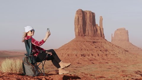 Woman hiker, backpack traveler camper looking at smartphone camera on top of mountain at sunset. Beautiful red rocks landscape view. Outdoor travel and online connection. Tourism 4K slow motion video
