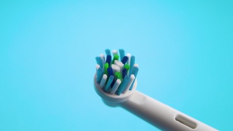 Electric dental toothbrush with bright colored bristles shakes in slow motion on a blue background. Macro shot