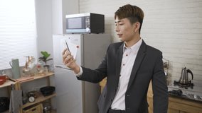 cheerful Asian man in business wear is touching hair and sipping tea while having online virtual chat with friend on the mobile phone in the morning before work at home
