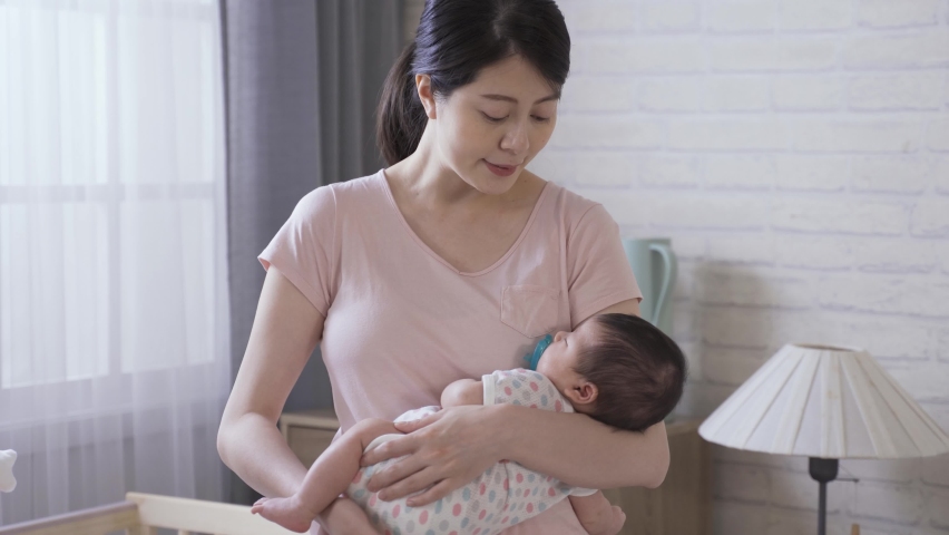 Korean mom is singing songs to her young child while patting her softly on the butt during nap time at home with white brick wall in the background. Royalty-Free Stock Footage #1076624102