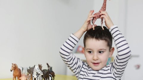 Caucasian toddler child playing with animal figurines toys in light room interior