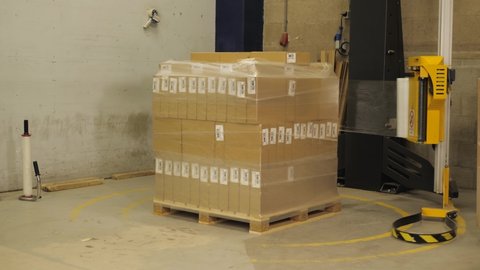 Machine wraps plastic around pallet with cardboard boxes in a factory