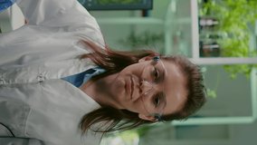 Vertical video: Pov of chemist woman in white coat analyzing with biologists team during online videocall meeting while sitting in microbiology lab. Specialist researching genetic mutation developing