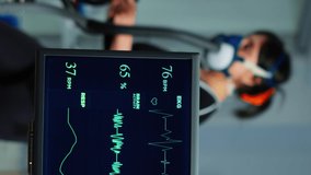 Vertical video: Medical researcher examining EKG image showing on monitor while patinet with mask running on cross trainer testing heart rate using electrodes.Doctor monitoring physical endurance in