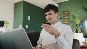 Mixed race male online shopping holding credit card sitting on sofa while typing on laptop 