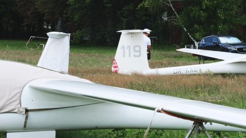 Man is preparing and checking gliders parked in the field, ready to fly. Small aviation extreme sport leisure activity. Washing small plane. Buzova, Kyiv, Ukraine - 07.07.2021