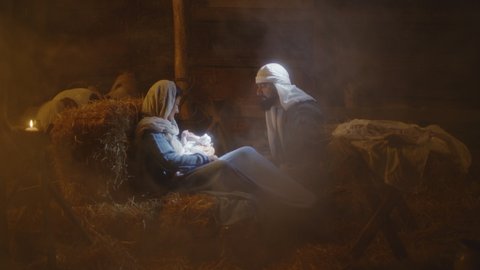Zoom in view of Joseph talking with Mother Mary and touching son of God in dark inn stable in Bethlehem