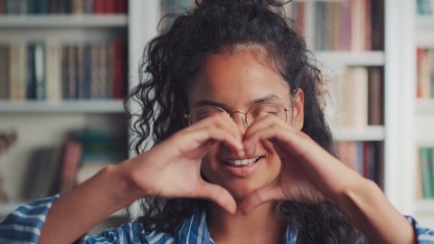 Close up of smiling young Indian woman volunteer showing hands sign heart shape looking at camera. Healthy heart health life insurance, love and charity, voluntary social work, organ donation concept.