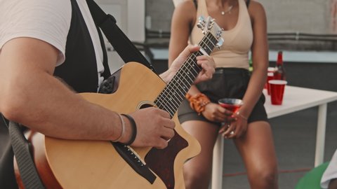 Close up slowmo of unrecognizable man playing acoustic guitar at party outside