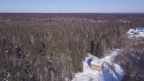 Top view of house on background of winter forest. Clip. Rustic cottage in middle of woods on sunny winter day. House near endless pine forest reaching to horizon
