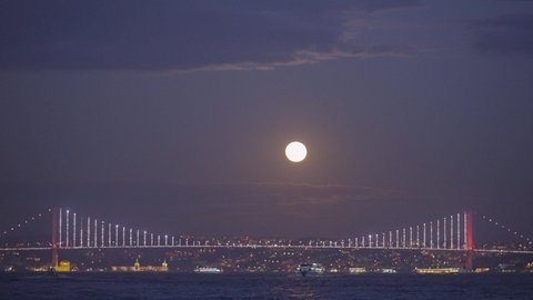 Sea landscape with shining city on background of evening sky with moon. Action. Beautiful coast on horizon with shining evening city. Moon over evening lights of city by sea