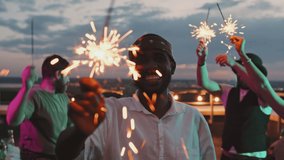 Slowmo shot of happy African-American man with sparkler smiling for camera at rooftop party on summer evening - Powered by Shutterstock - Get 15% off with code: PIKWIZARD15