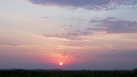 Beautiful Sunset over the Horizon in the Field, Colorful Sky and Clouds at Sunset, Time Lapse. The Sun Sets over the Horizon, Illuminating the Sky and Clouds with Rays. Nature 4K, Timelapse.